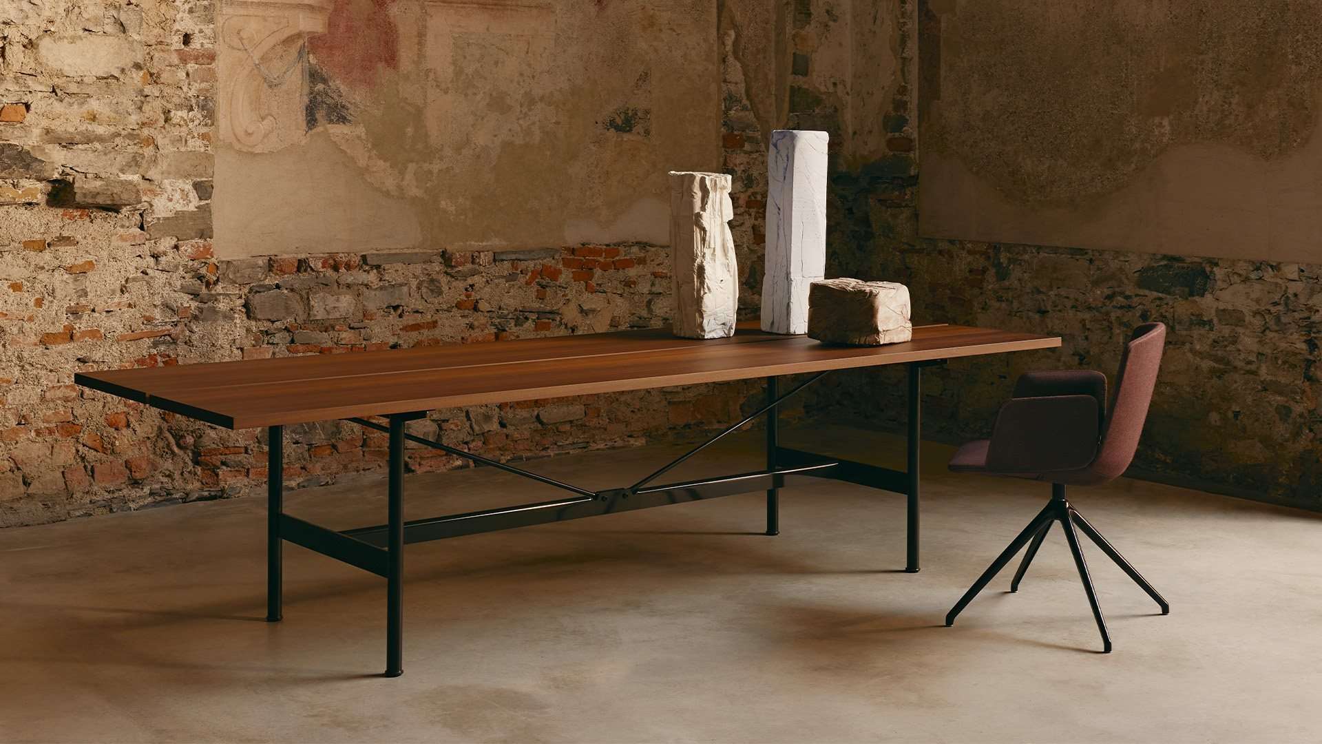Long timber table on a black steel frame in a room with raw plaster walls