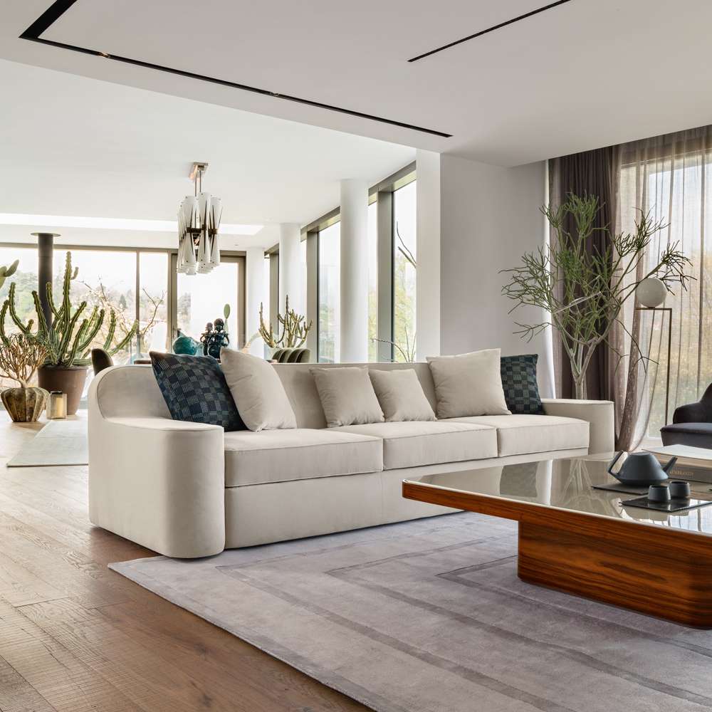 Long cream sofa and a walnut coffee table in a bright room with tall plants