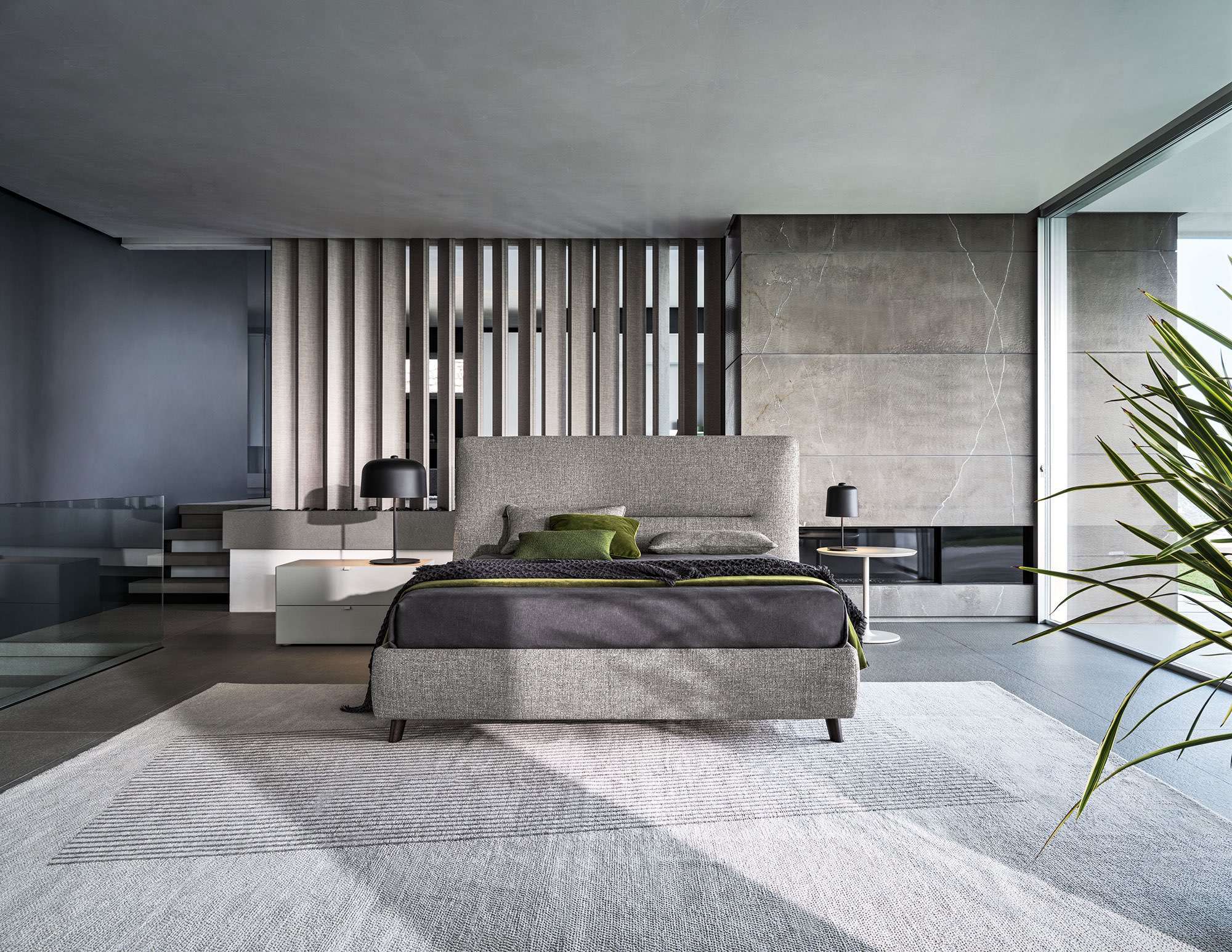 Bed in grey fabric in an open room with timber screens and a fireplace