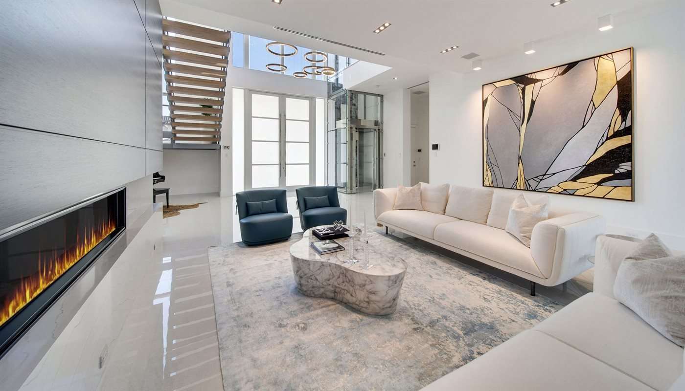 White sofa and blue armchairs around a sculptural table in a double-height room with a fireplace