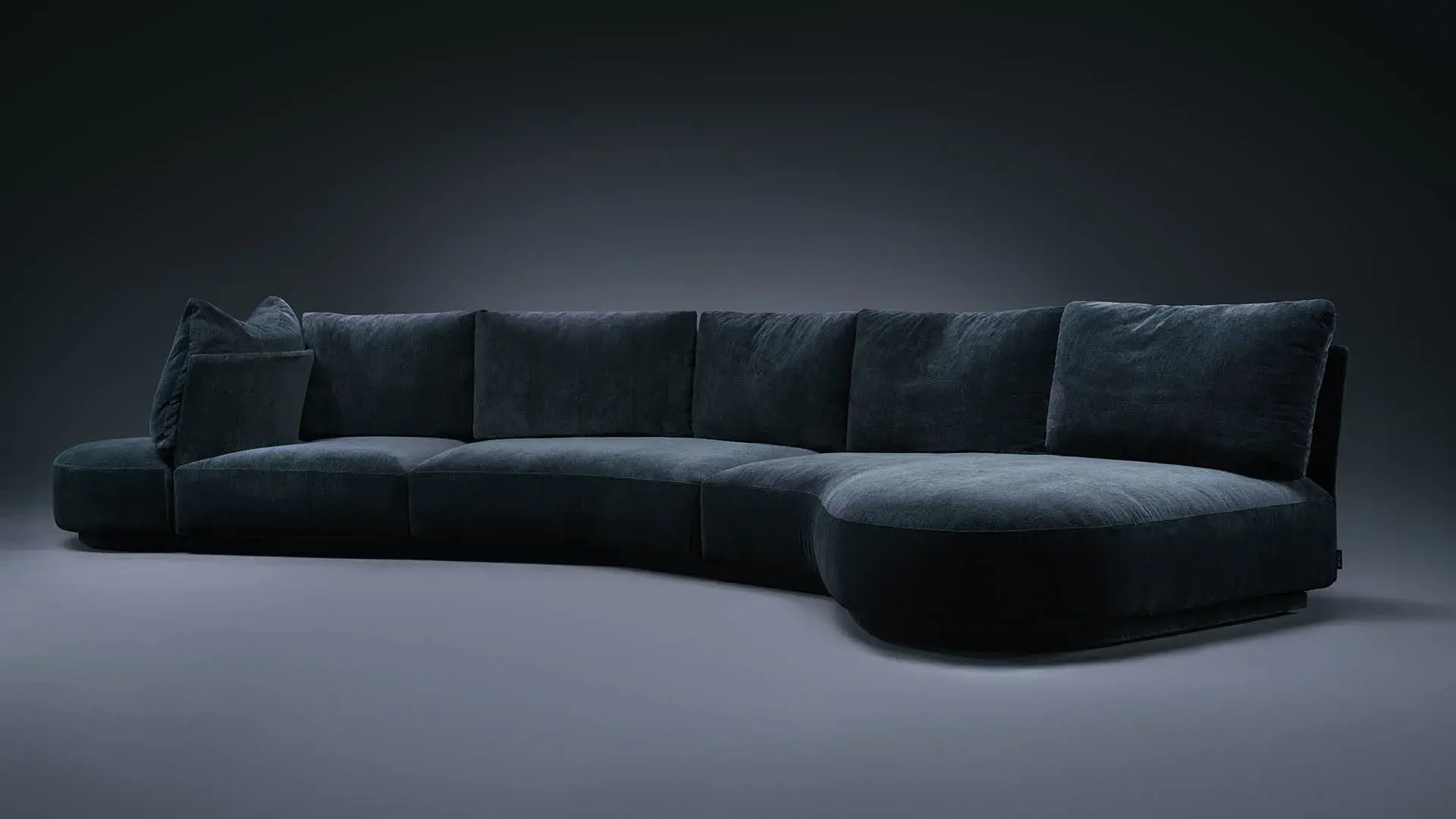 Curved modular sofa in deep blue velvet on a dark studio set