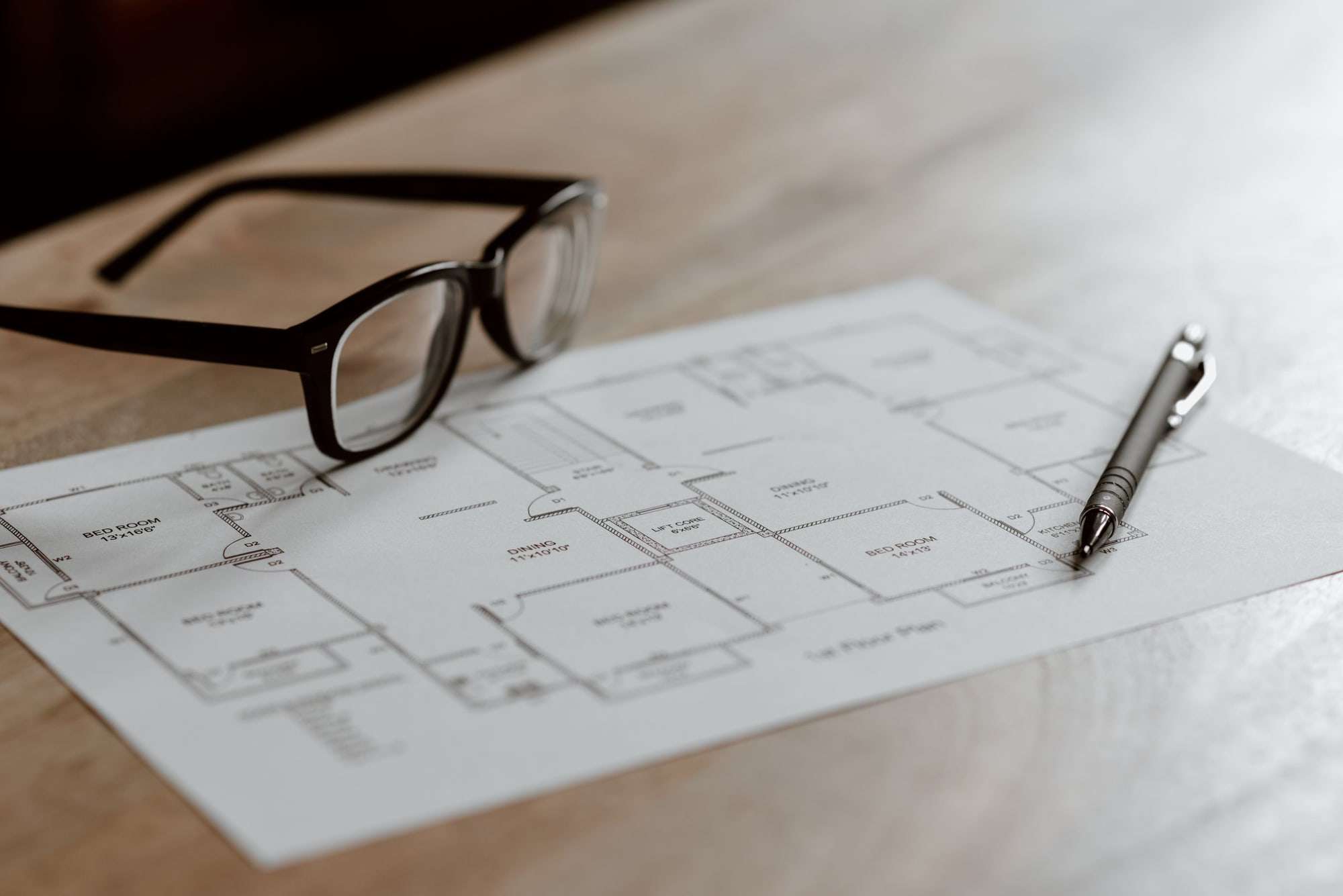 Floor plan on a pale table with reading glasses and a pen