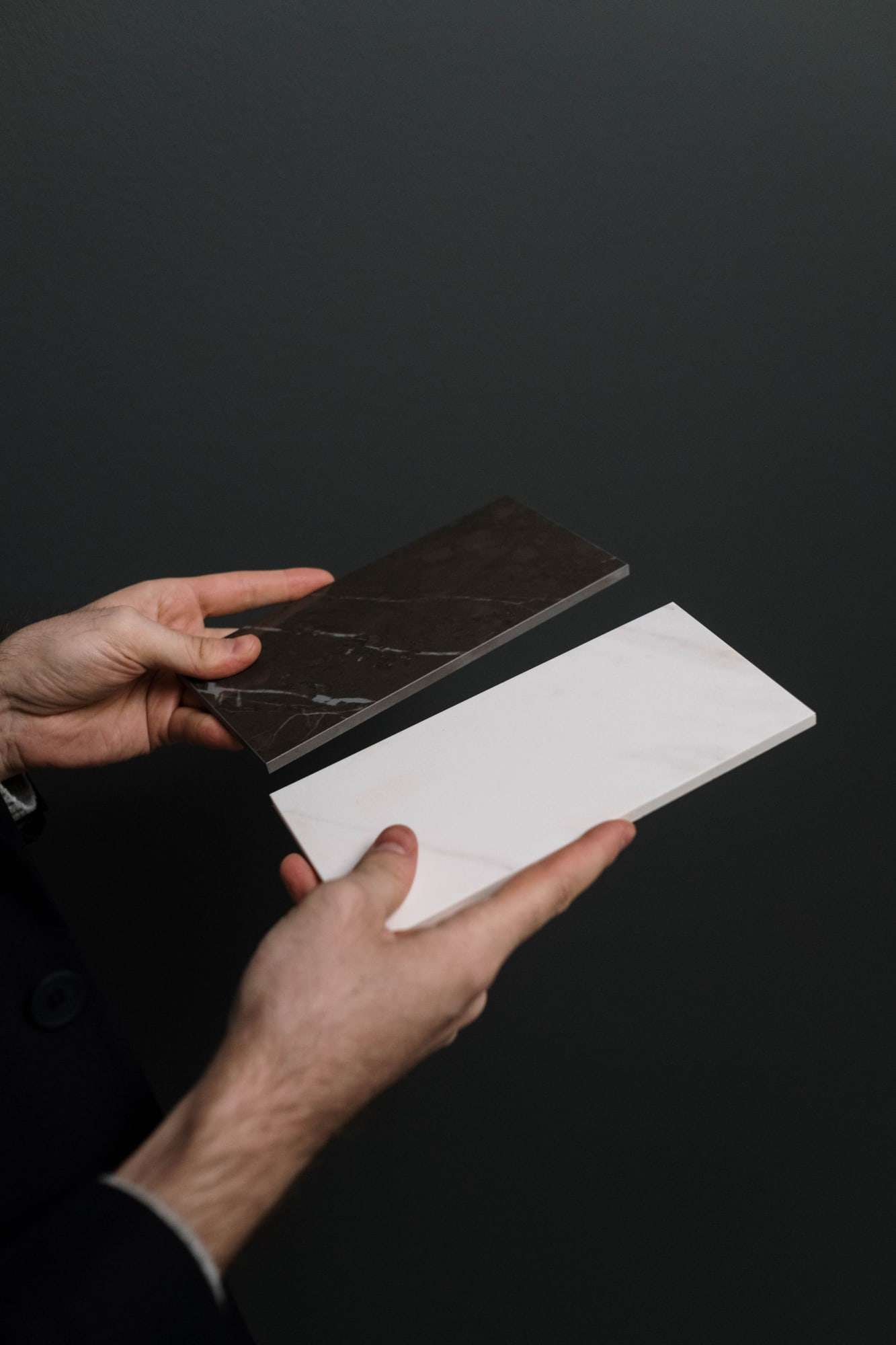 Hands holding a black and a white marble sample against a dark background