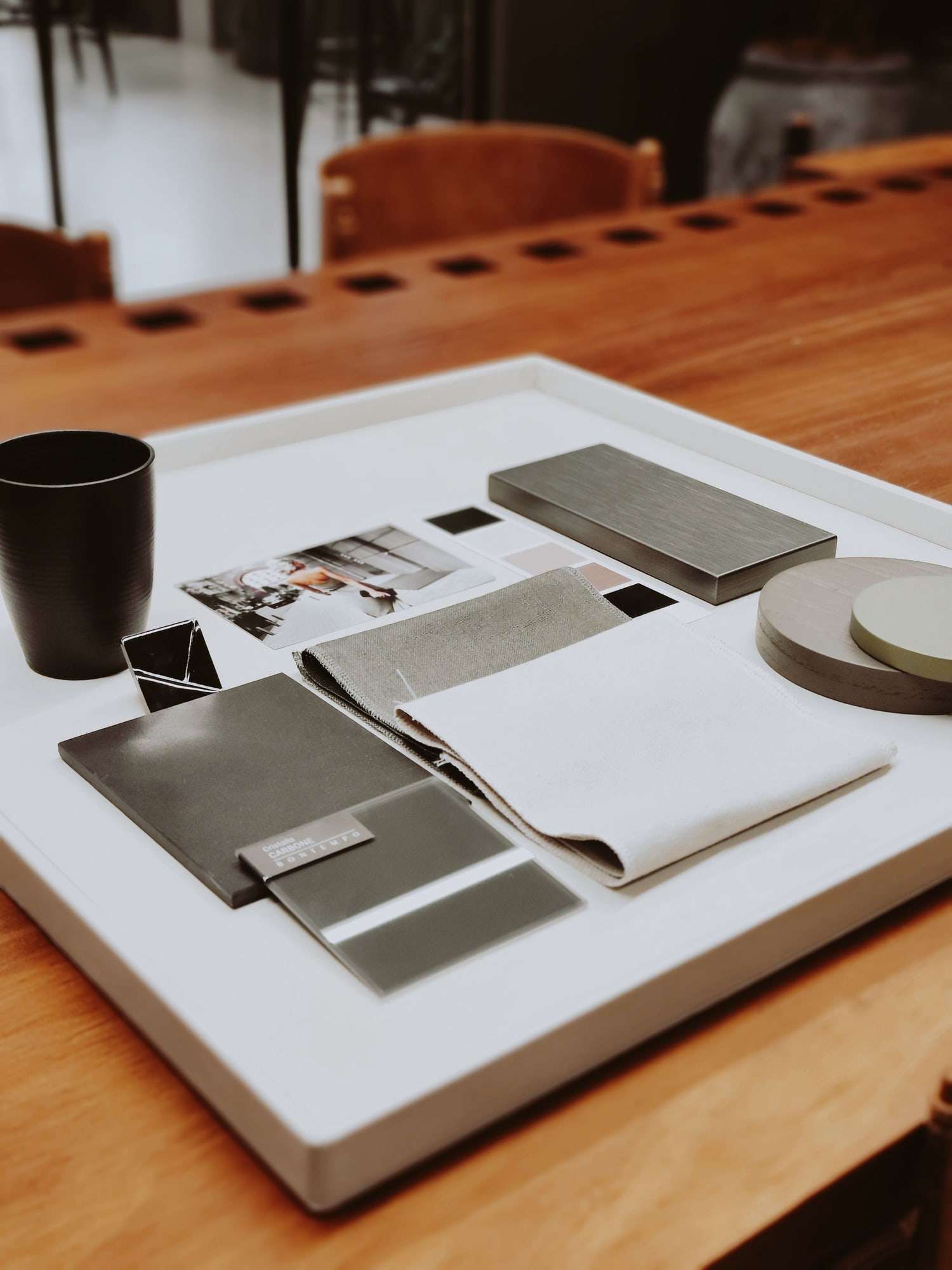 Tray of fabric, leather and metal samples beside a cup and small photographs on a wooden desk