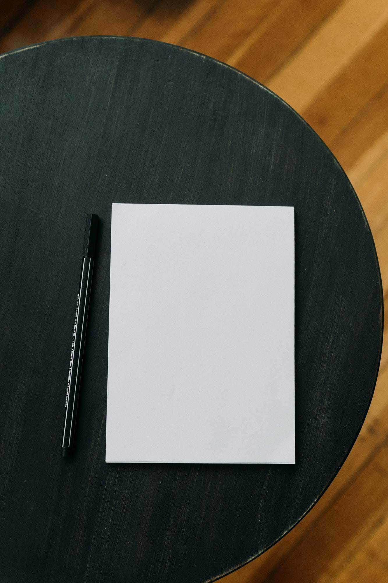 A single blank sheet and a black pen on a dark round table