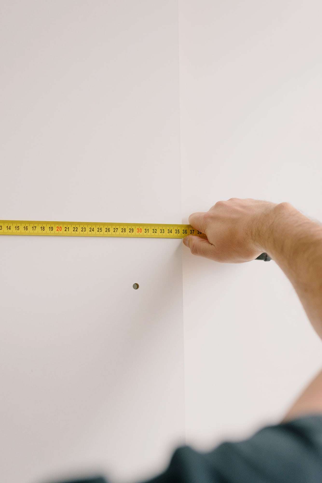 Hand pulling a tape measure along a white wall