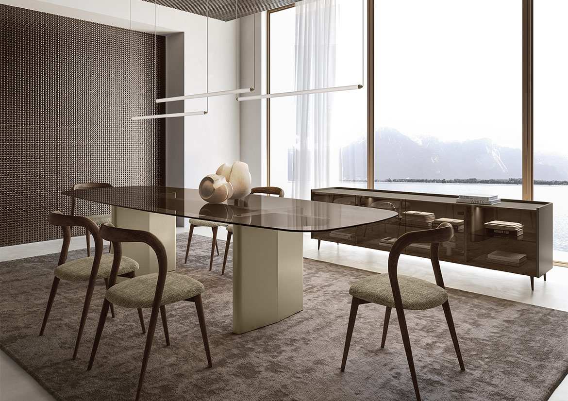 Dining table with a bronze glass top and curved timber chairs beside a tall window over a lake